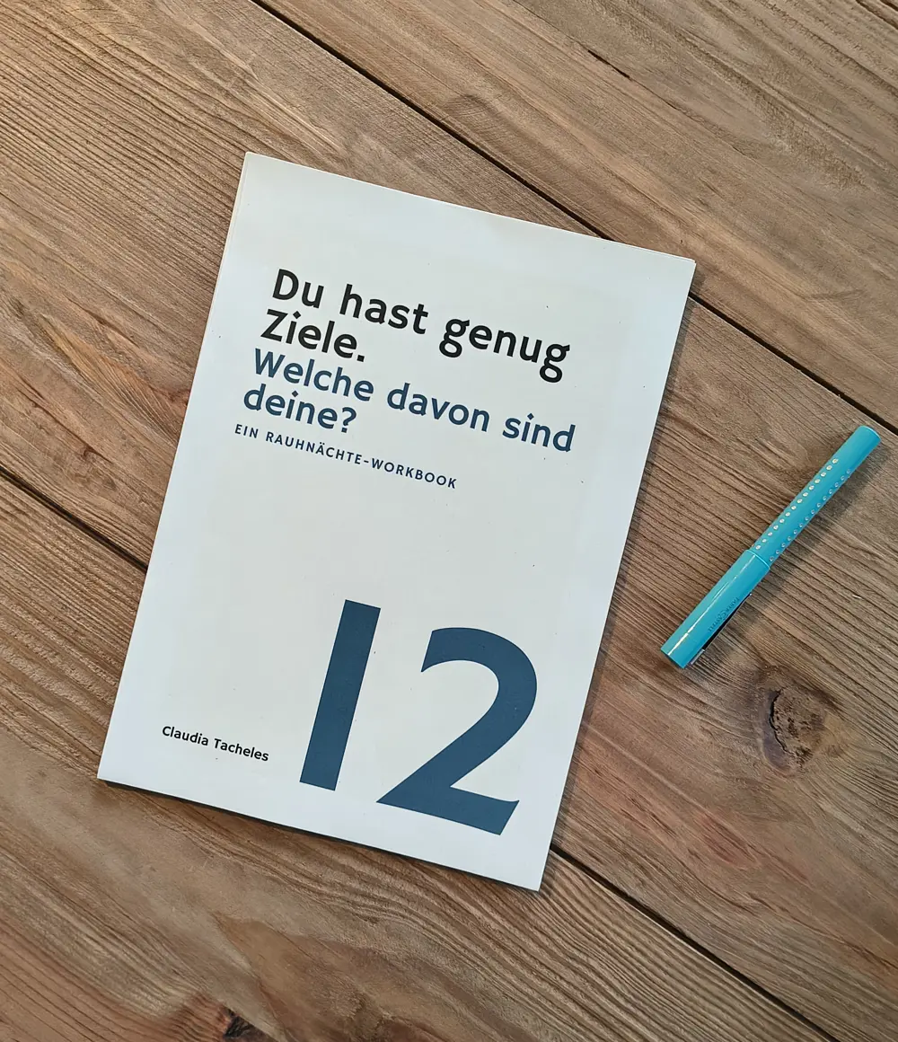 Das ausgedruckte Rauhnächte-Workbook liegt auf einem Holztisch, daneben ein türkiser Stift